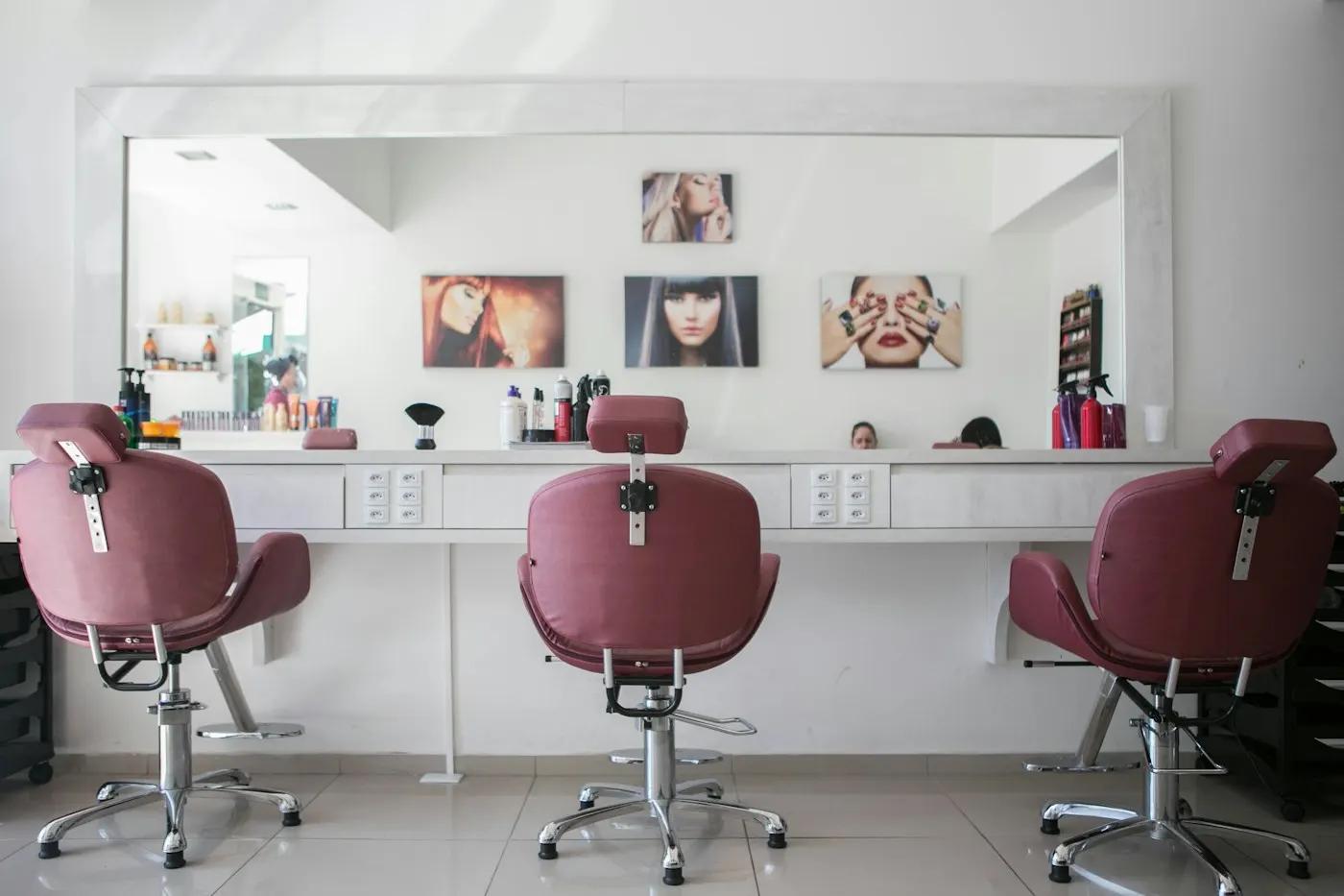 Beauty salon styling stations with pink chairs and a long mirror